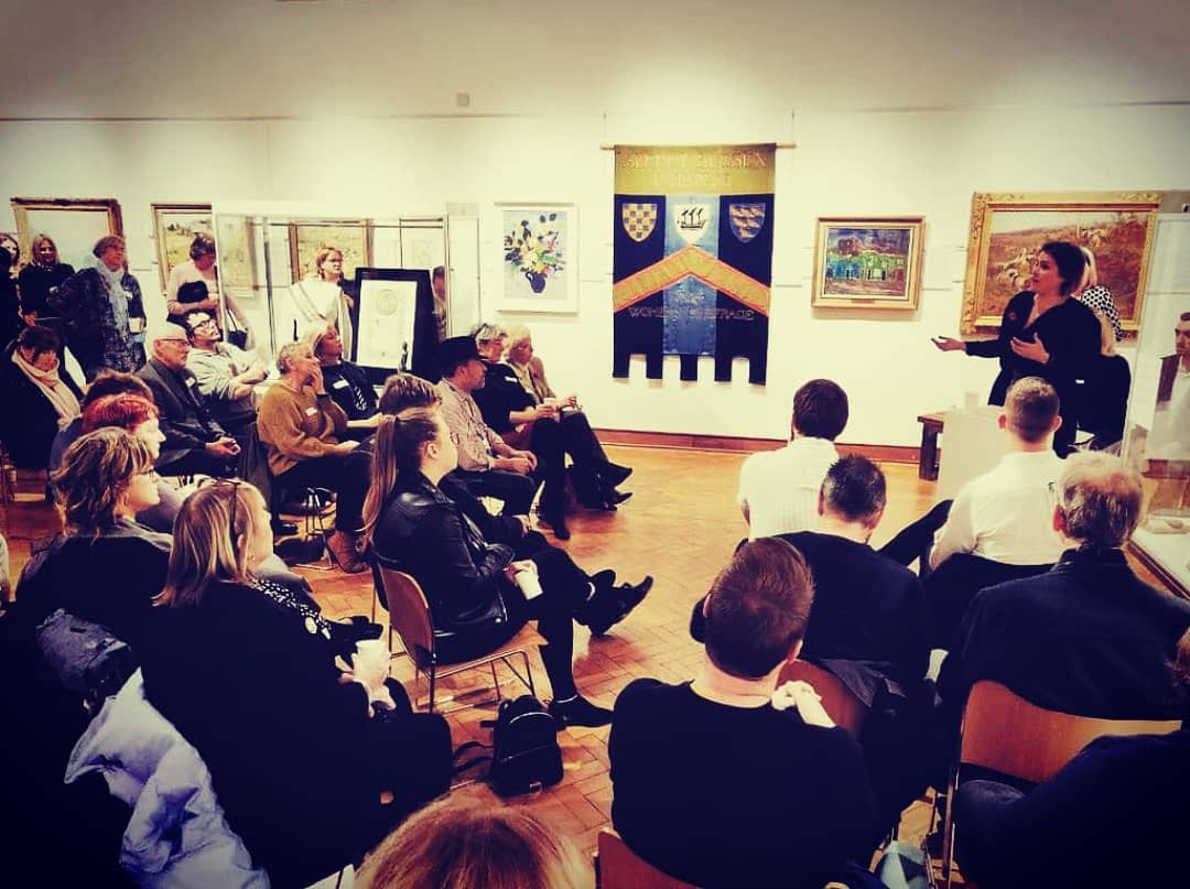 An audience of people listening to a talk in an art gallery